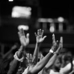A group of people raising hands in a black and white concert setting, showing unity and celebration.